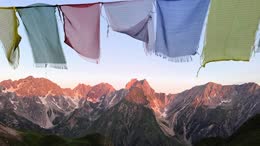 Bunte Stoffbänder vor Alpenpanorama im Sonnenaufgang.